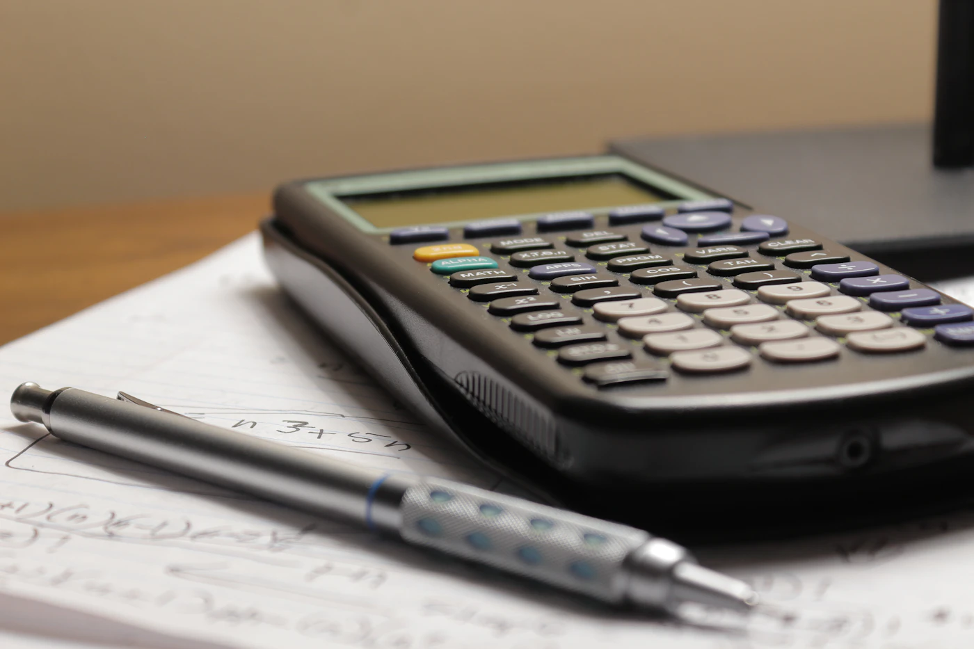 A calculator and pen resting on a page of handwritten calculations