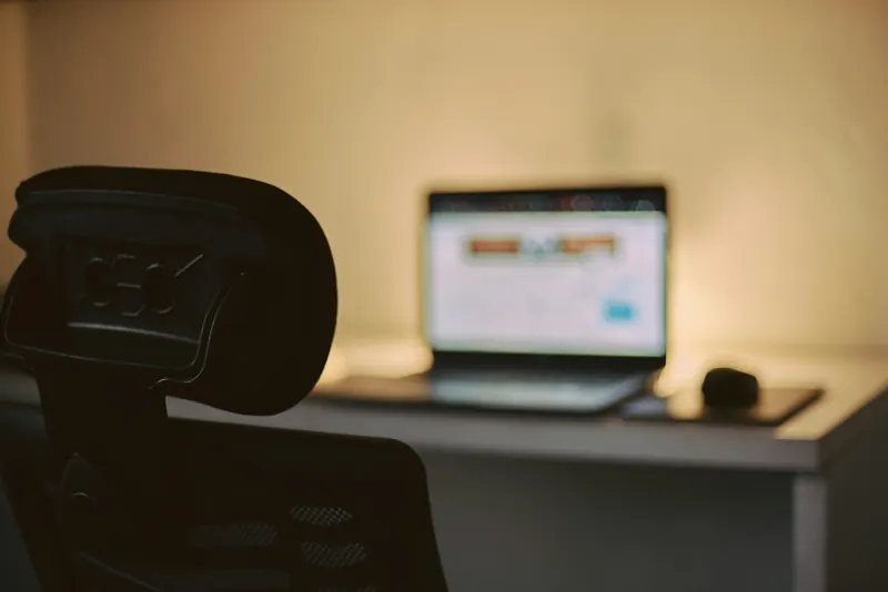 A tidy desk with an open laptop and lamp at dusk